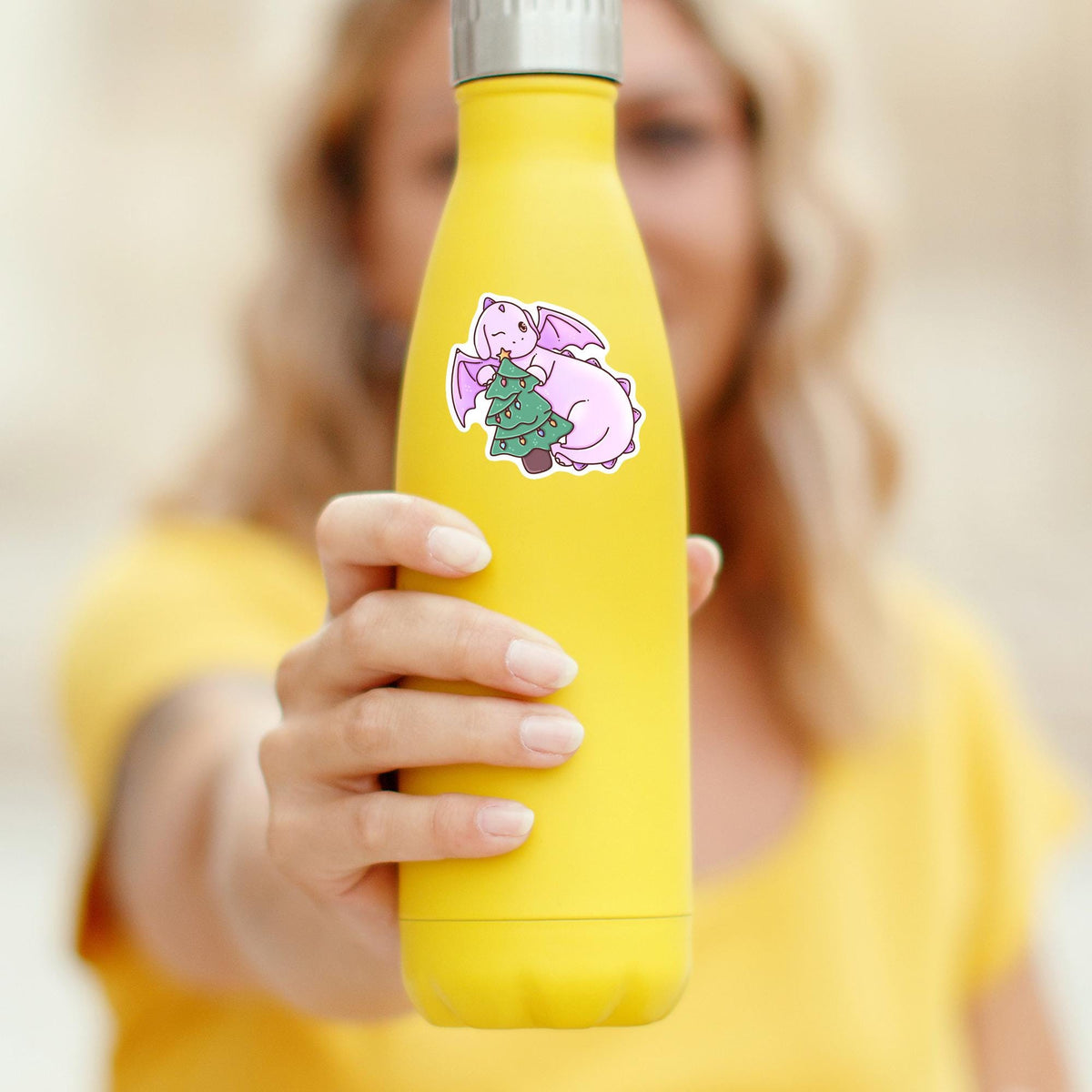 Christmas Tree Dragon waterproof sticker on a yellow water bottle held by a smiling woman, cute holiday vinyl decal for tumblers and bottles