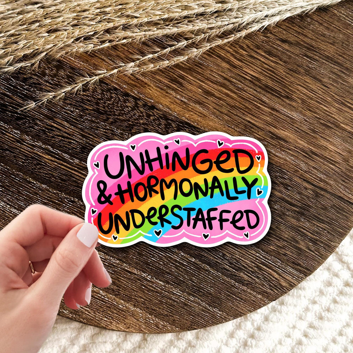 Unhinged and Hormonally Understaffed rainbow vinyl die-cut sticker held in a hand, funny sarcastic quote decal, waterproof gift for moms and chaotic girlies