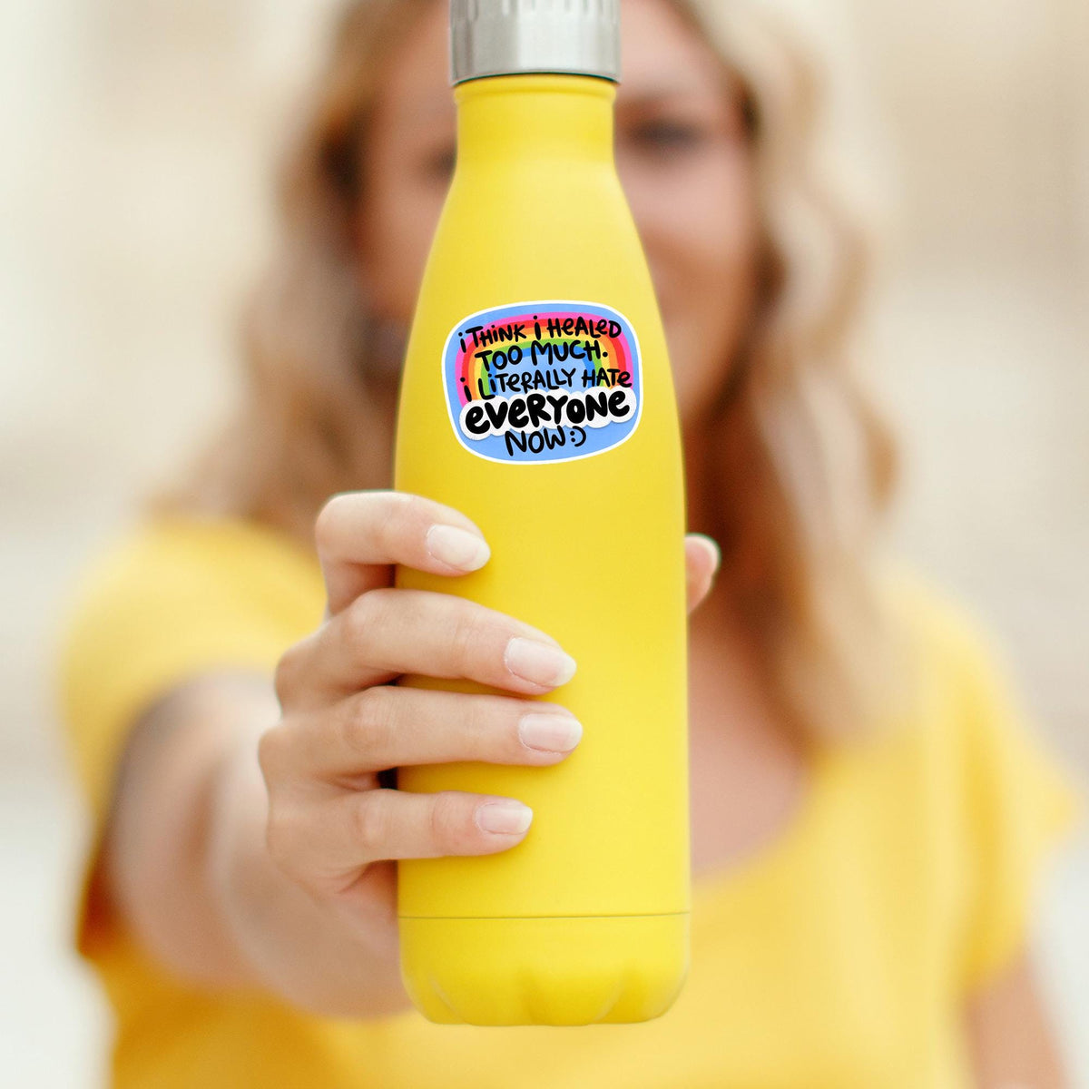 Hand holding a yellow water bottle with the Healed Too Much rainbow sticker, waterproof vinyl decal, funny grumpy girlie quote gift for tumbler decor