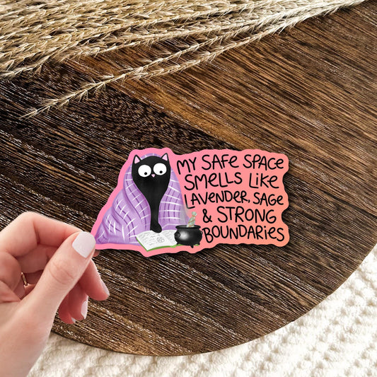 Black cat in a lavender blanket sticker reading my safe space smells like lavender, sage and strong boundaries, held in hand on wood