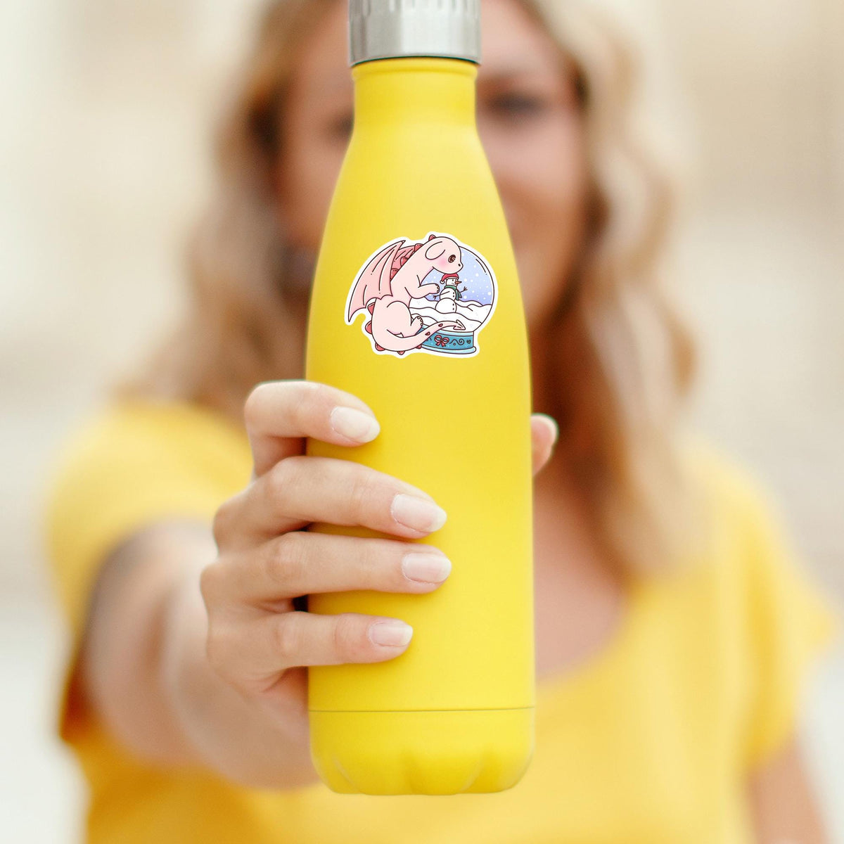 Snow Globe Dragon waterproof sticker on a yellow water bottle held by a woman, durable vinyl decal for tumblers and bottles